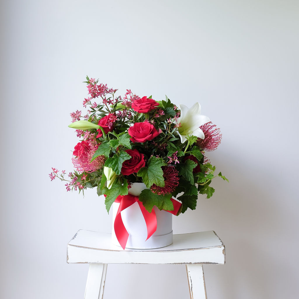 Celebrate Christmas with our Noel Hat Box Arrangement featuring lilies, holly, spruce & berries. Custom colours available. Same-day Melbourne delivery.