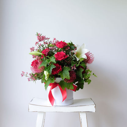 Celebrate Christmas with our Noel Hat Box Arrangement featuring lilies, holly, spruce & berries. Custom colours available. Same-day Melbourne delivery.